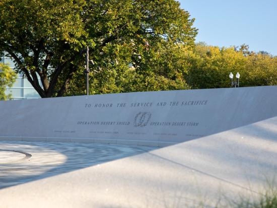 White stone memorial wall shaded by green trees. 