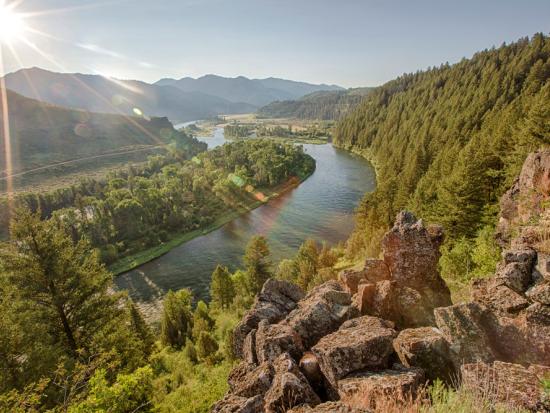 Rocky cliff above winding river, surrounded by mountain landscape. 