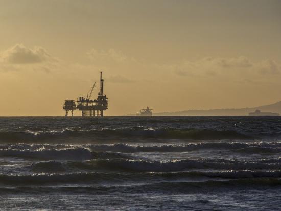 Oil rigs in the distance with waves crashing on the shore.