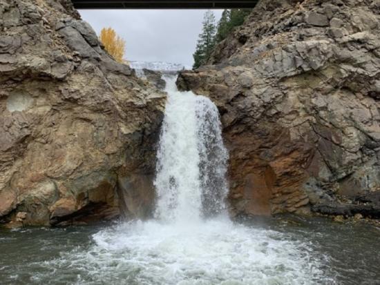A small waterfall flowing through brown rocks with a gray bridge in the background