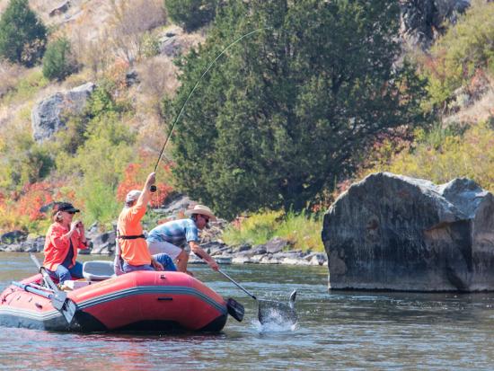 Three recreationists are fishing on a river in a red boat