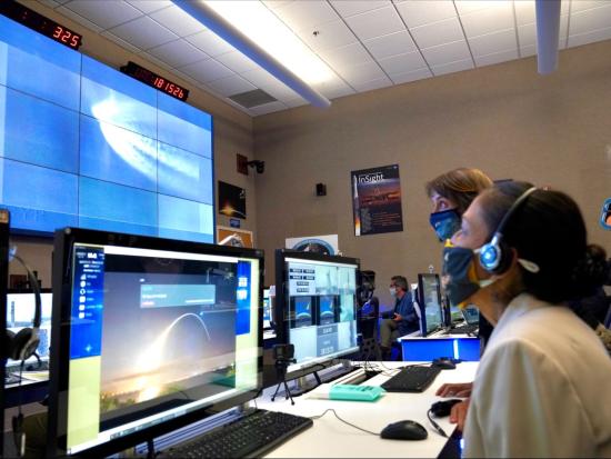 Secretary Haaland sits at a desk with a computer while wearing a mask during the Landsat 9 launch.