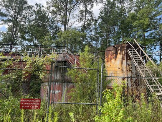 Orphaned Well surrounded by overgrown weeds and a chain-link fence. 