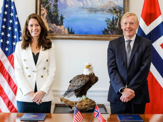 Kate MacGregor and a white male Norwegian official stand in front of their national flags.