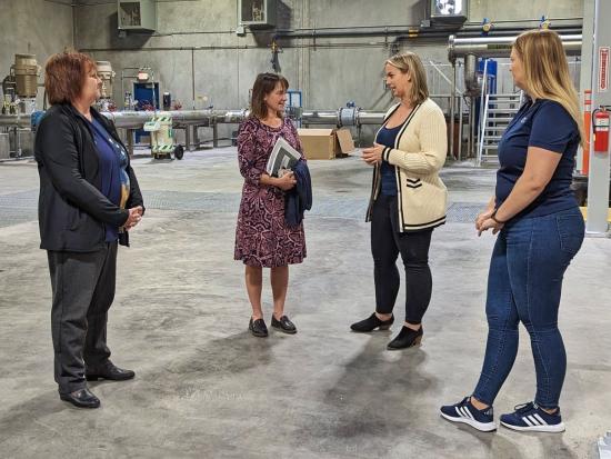 Four women are standing and talking in a water recycling facility