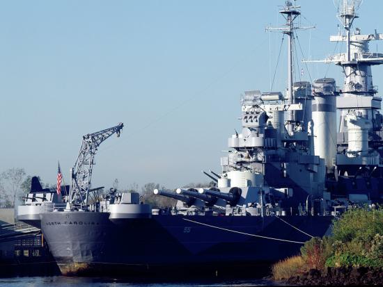 A large metal battleship is tied up next to a dock.