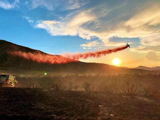 An airtanker drops red retardant on a wildland fire at sunset