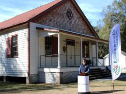 NPS Director Sams stands in front of a white podium before an old white house with red trimmings and a red roof