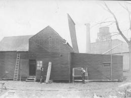 A historic photo of black papered building used as a film studio with workers nearby. The original "Black Maria" with several Edison employees.