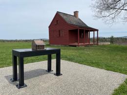 Bronze model of a house sits on a black table in front of a red wooden house