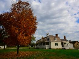 White building with shingle roof among fall colored trees.