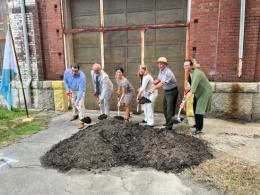 Group of people with shovels stand in front of dirt at a construction site