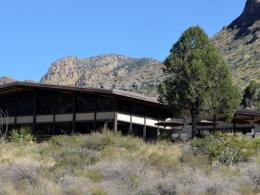 A dark brown building surrounded by mountains and green and grey shrubs. 