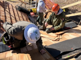 Three people in uniform and safety equipment doing work on top of a roof.