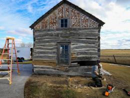 Man wearing hard hat, gloves, and chaps performs historic cabin restoration work.