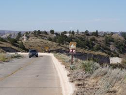 A vehicle drives on a concrete-surfaced road with bluffs in the background.