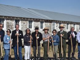 A group of 10 people stand in a line facing forward while holding shovels.