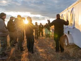 Group of firefighters standing around trailer during morning sunrise meeting.
