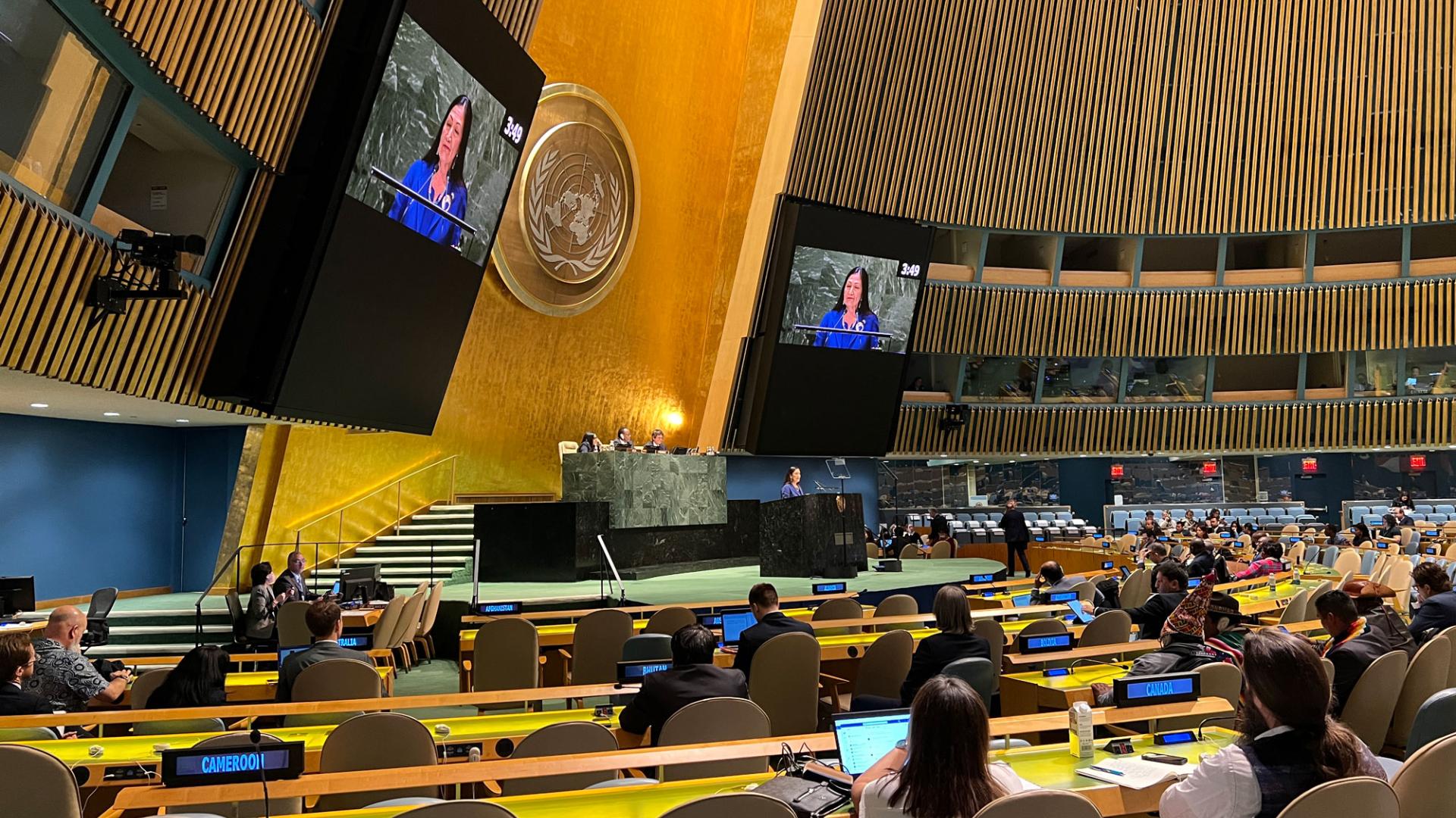 Large gold colored conference room with two TV screens featuring Secretary of the Interior Deb Haaland.