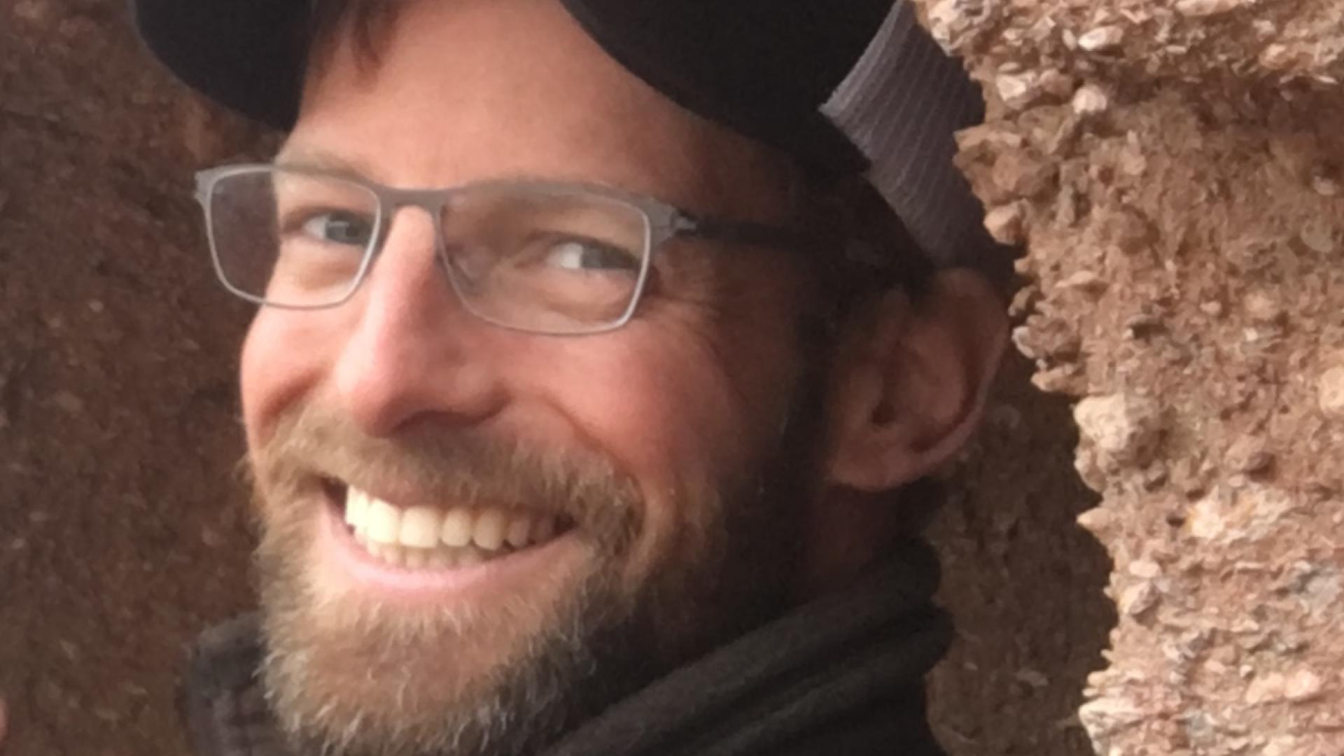 Nate Matthews smiles at the camera from a rock alcove